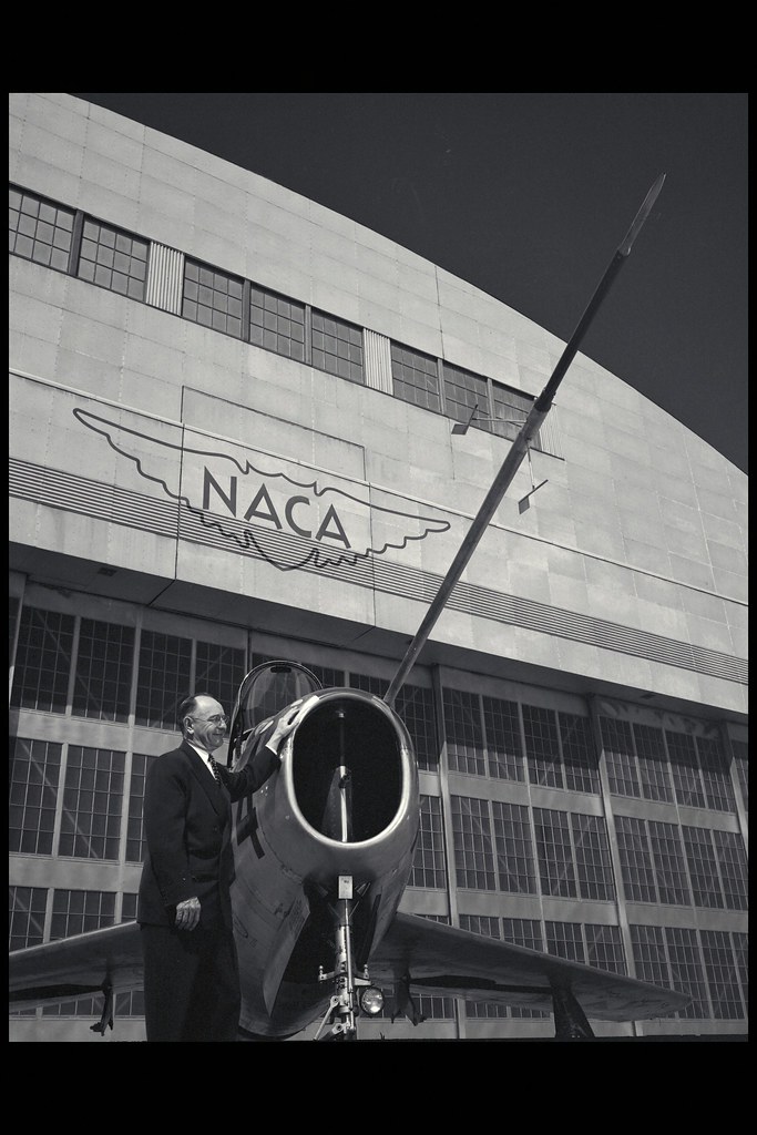: Smith J. DeFrance poses by a Republic F-84 aircraft on flight line at Ames Research Center. Note the classic National Advisory Committee for Aeronautics (NACA) wings logo on the hangar.