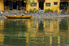 Yellow building reflected in river with bicycles and cyclist.