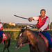 Horse rider holding a saber in hand. Additional riders in blurry background