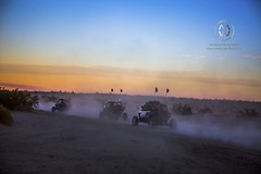 A group of off road vehicles line up to race across the desert in sunset.