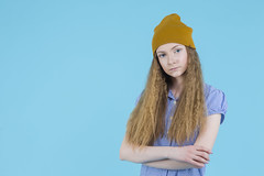 Serious Caucasian Teenage Girl In Long Blue Dress, Wellington Rubber Boots Posing In Winter Hat With Hands Folded