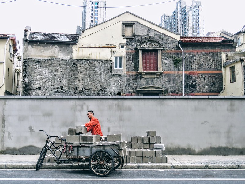 In front of the wall of a vacant lot where a demolished century-old building once stood, a demolition worker carries the extra hollow bricks onto a tricycle to be transported to other empty buildings that have not yet been demolished.<br/>© <a href="https://flickr.com/people/49585343@N00" target="_blank" rel="nofollow">49585343@N00</a> (<a href="https://flickr.com/photo.gne?id=51442905766" target="_blank" rel="nofollow">Flickr</a>)