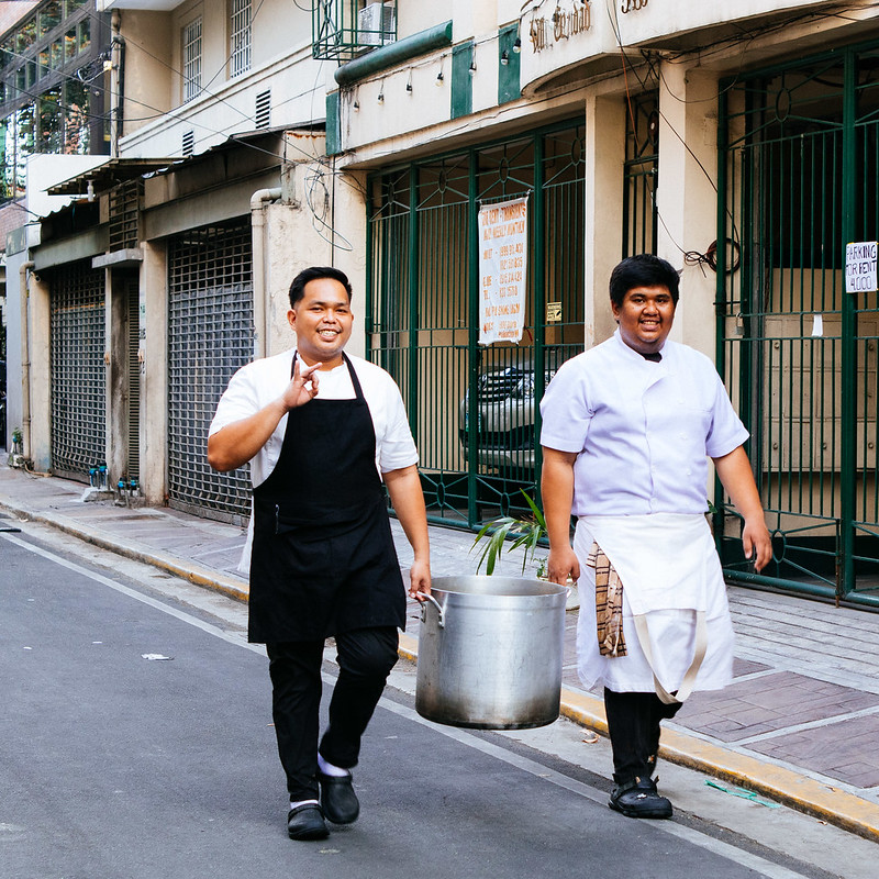 kitchen staff carrying a pot on Enriquez St.<br/>© <a href="https://flickr.com/people/37837114@N00" target="_blank" rel="nofollow">37837114@N00</a> (<a href="https://flickr.com/photo.gne?id=52757200556" target="_blank" rel="nofollow">Flickr</a>)