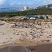Drone shot of tourists at a busy sandy beach on vacation with Silos of Lisbon in the background