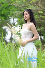 A beautiful girl with curly black hair adorned with flowers, radiating in a pure white dress, captivates with white daisies in hand, a serene moment in the heart of spring.