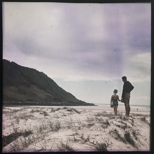 Man with a young girl in her swimmers on the sand dunes of a Gold Coast beach in the 1940s
