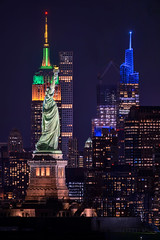 View of the Statue of Liberty, the Empire State Building and the SUMMIT One Vanderbilt building at night.