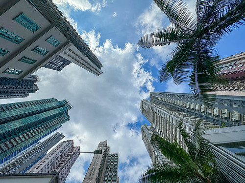 Looking up to the top of skyscrapers and tall apartment buildings with a blue and cloudy sky in a residential area of Hong Kong