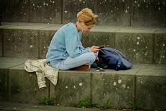 Germany - a woman sitting on the steps looking at her cell phone, a photo, by Hans Schwarz, pixabay, blue sweater, chalk, studious, !! very coherent!!, wearing a baggy, morning detail, joel fletcher, girl, highly detaild, spiralling