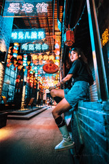 Young woman sitting on a ledge in a neon-lit alleyway