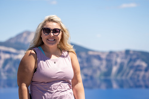 Stylish but casual blonde woman poses with sunglasses and a tank top at Crater Lake National Park Or