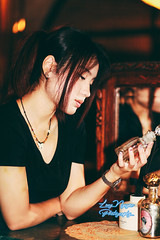 A beautiful girl stands at a wooden table in the corner of a room filled with nostalgic items, with a soft, dim light from an electric lamp in the background. The photo uses the warm, rich tones of Kodak Gold 200 film, giving it a classic and vintage feel