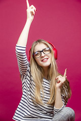 One Excited Dancing Blond Girl in Striped Casual Clothing Posing In Headphones With Lifted Hands Over Crimson Red