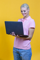 Portrait of Calm Caucasian Young Blond Girl Holding Laptop Computer and Working Typing Text Chatting Isolated over Yellow background